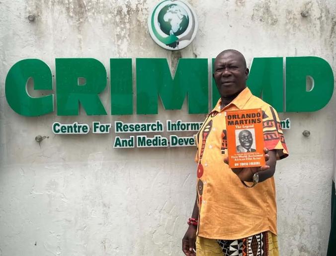 Dr Raphael James holding a copy of a book on Pa Orlando Martins